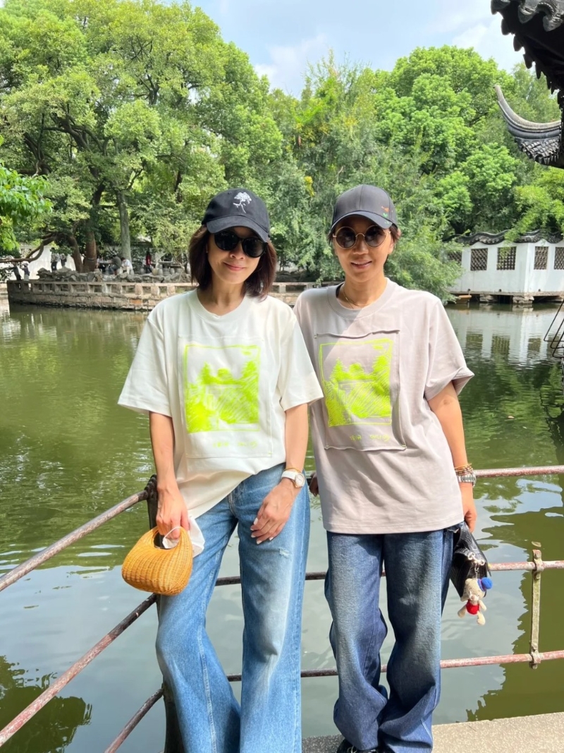 劉嘉玲頭戴黑色cap帽，身穿一件印有螢光圖案的白色短袖T恤、淺藍(lán)色牛仔長褲，身上拎住一個編織包包，非常休閑地在園林影靚相。