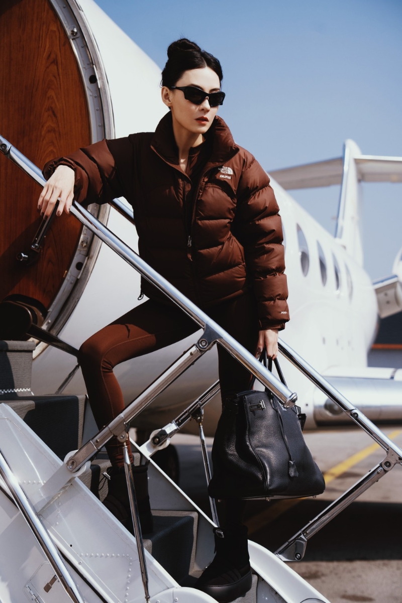 扎起丸子頭的張栢芝身穿一件棕色羽絨服及同色貼身連體衣，再配上黑色短靴及墨鏡，完美地襯托出她的纖幼身形，整體造型既保暖又充滿時尚氣息。