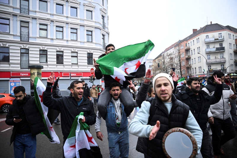 2024年12月8日，德國柏林?jǐn)⒗麃喎纯管娦纪品瓟⒗麃啺⑺_德政府后，人們舉著敘利亞反對派旗幟聚集在柏林一處廣場。 路透社