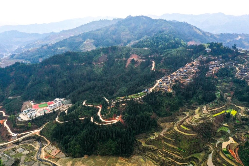 圖為群山環(huán)抱的貴州省大歹苗寨（右）及大歹小學(xué)（左）