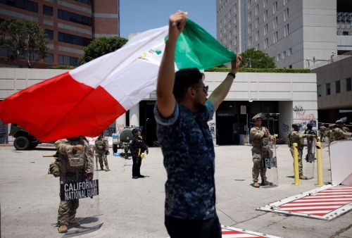 1名男子10 日高舉墨西哥國旗，在洛杉磯市中心的加州國民警衛(wèi)隊成員面前抗議。路透社
